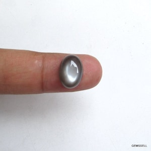 May include: A gray oval cabochon gemstone with a white iridescent sheen.