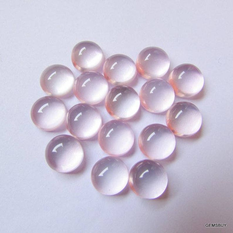 May include: A collection of 18 round, pale pink cabochon gemstones. The stones are smooth and polished, with a translucent appearance.