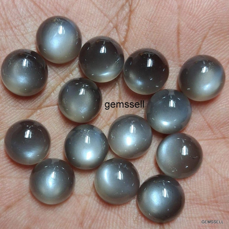 May include: A collection of 15 round, gray moonstone cabochons with a silvery sheen. The stones are smooth and polished, with a slight iridescent effect.