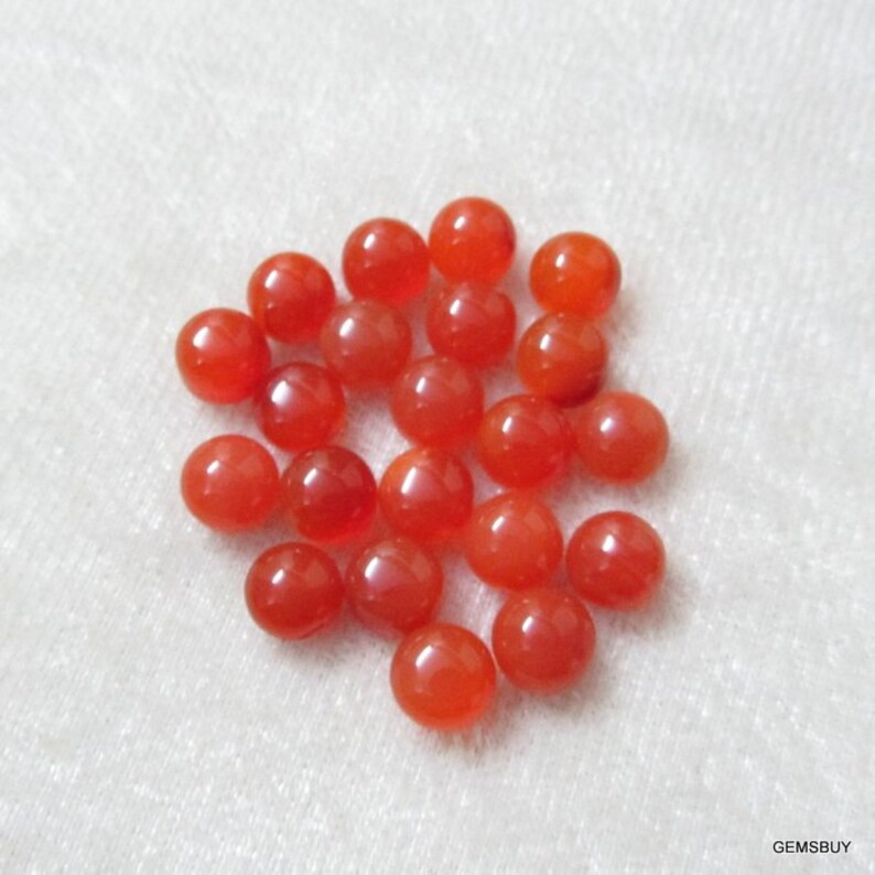 May include: A pile of 25 round, orange carnelian gemstones. The stones are smooth and polished, and they are all about the same size.