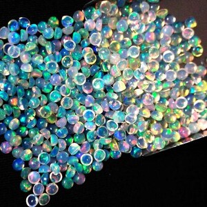 Op de afbeelding: Een stapel iriserende opaal cabochons in verschillende tinten blauw, groen en wit. De cabochons zijn rond en hebben een glad, gepolijst oppervlak.
