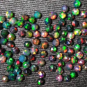 Puede incluir: Una colecci&oacute;n de piedras preciosas de &oacute;palo negro iridiscente, cada una con un patr&oacute;n &uacute;nico de colores verde, rojo y azul. Los &oacute;palos est&aacute;n facetados y tienen una forma puntiaguda.
