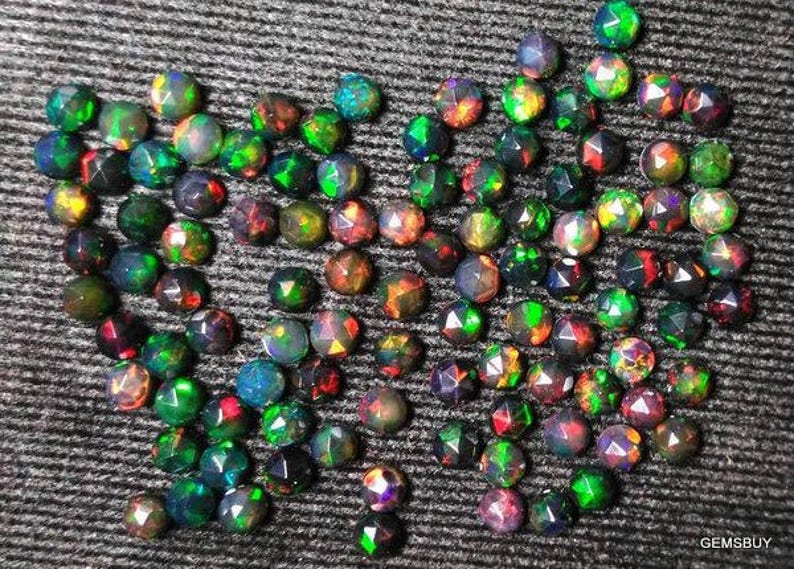 Puede incluir: Una colecci&oacute;n de piedras preciosas de &oacute;palo negro iridiscente, cada una con un patr&oacute;n &uacute;nico de colores verde, rojo y azul. Los &oacute;palos est&aacute;n facetados y tienen una forma puntiaguda.