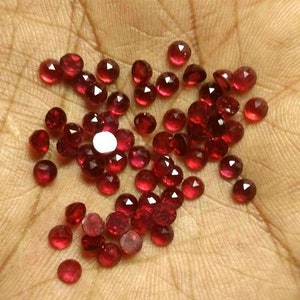 May include: A collection of small, faceted, red gemstones. The gemstones are scattered on a hand.