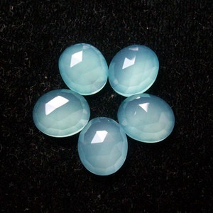 May include: Five light blue chalcedony gemstones, each with a smooth, faceted surface, arranged in a starburst pattern on a black background.