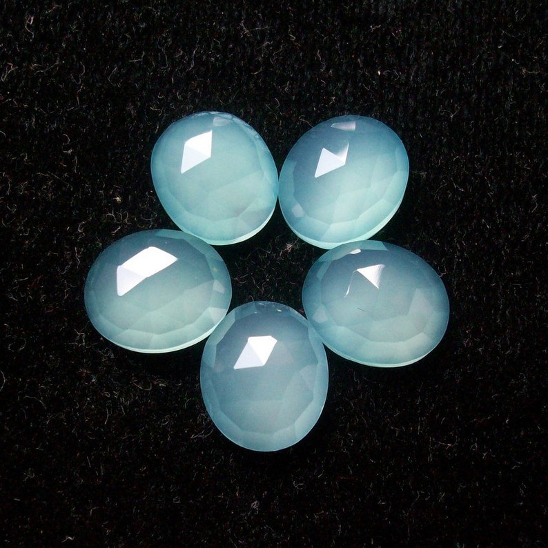 May include: Five light blue chalcedony gemstones, each with a smooth, faceted surface, arranged in a starburst pattern on a black background.