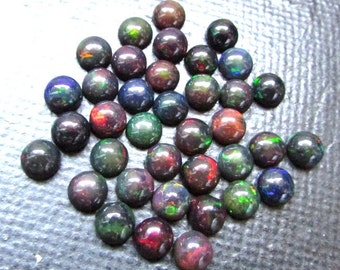 May include: A collection of 30 round black opal cabochons, each displaying a variety of iridescent colors, including green, red, blue, and purple.