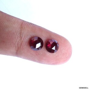 May include: Two round, red gemstones with faceted surfaces. The gemstones are approximately 5mm in diameter.