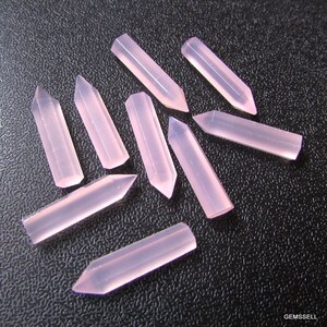 Puede incluir: Una colecci&oacute;n de diez puntas de piedras preciosas rosas, cada una con una punta facetada y una base rectangular. Las puntas est&aacute;n dispuestas en un patr&oacute;n aleatorio sobre una superficie negra.