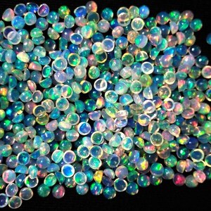 May include: A large group of iridescent opal cabochons in various shades of blue, green, and pink. The cabochons are round and have a smooth, polished surface.