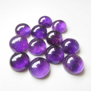 May include: A group of 12 round, purple amethyst cabochons. The cabochons are smooth and polished, with a deep purple color.