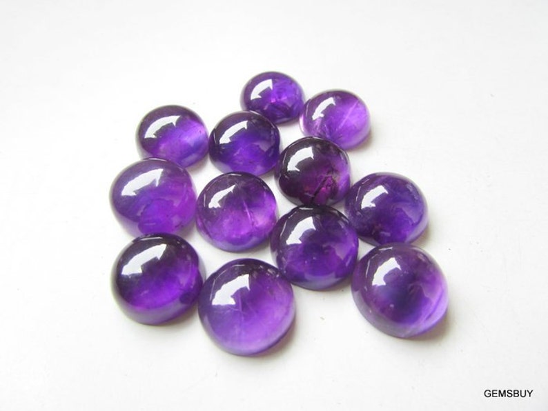 May include: A group of 12 round, purple amethyst cabochons. The cabochons are smooth and polished, with a deep purple color.