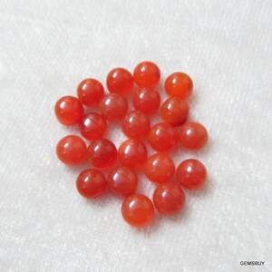 May include: A pile of 25 round, orange carnelian gemstones. The stones are smooth and polished, and they are all about the same size.