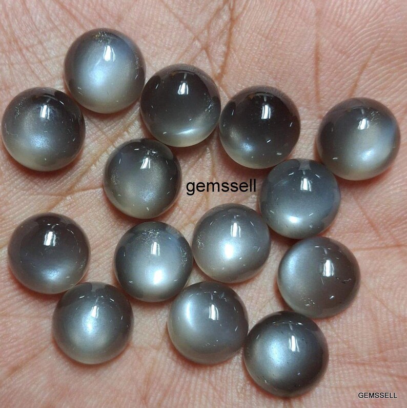 May include: A collection of 15 round, gray moonstone cabochons with a silvery sheen. The stones are smooth and polished, with a slight iridescent effect.