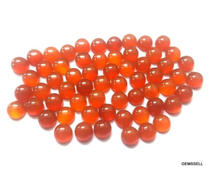 May include: A collection of round, orange carnelian gemstones. The stones are smooth and polished, and they are arranged in a loose pile.