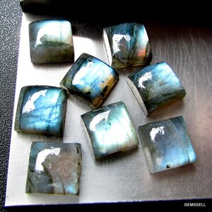 May include: A collection of nine iridescent blue-green labradorite gemstone cabochons, each with a unique pattern of light and dark shades.