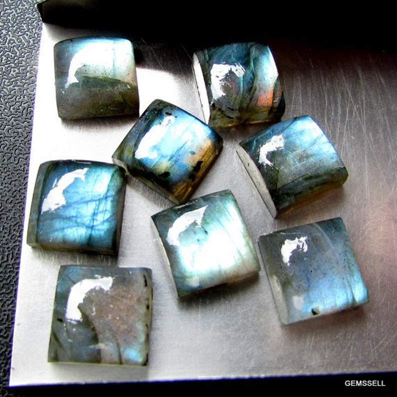 May include: A collection of nine iridescent blue-green labradorite gemstone cabochons, each with a unique pattern of light and dark shades.