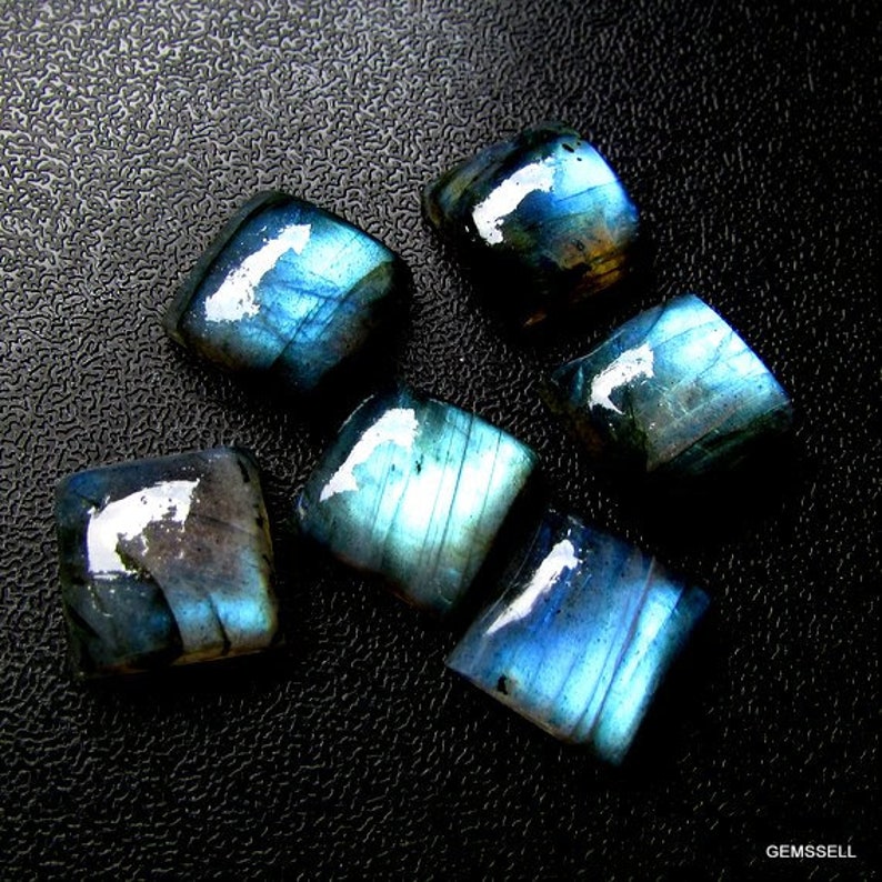 May include: Six iridescent blue labradorite gemstone cabochons, cut into square shapes, with a dark blue and black background.