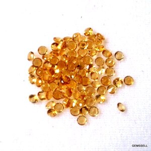 May include: A pile of small, round, orange gemstones. The gemstones are faceted and have a shiny, translucent appearance.