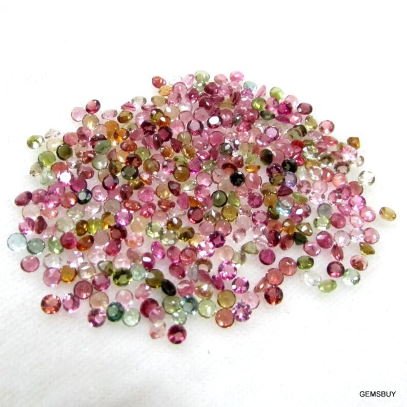 Puede incluir: Un mont&oacute;n grande de piedras preciosas redondas y facetadas en varios tonos de rosa, verde y marr&oacute;n. Las piedras preciosas est&aacute;n esparcidas sobre una superficie blanca.