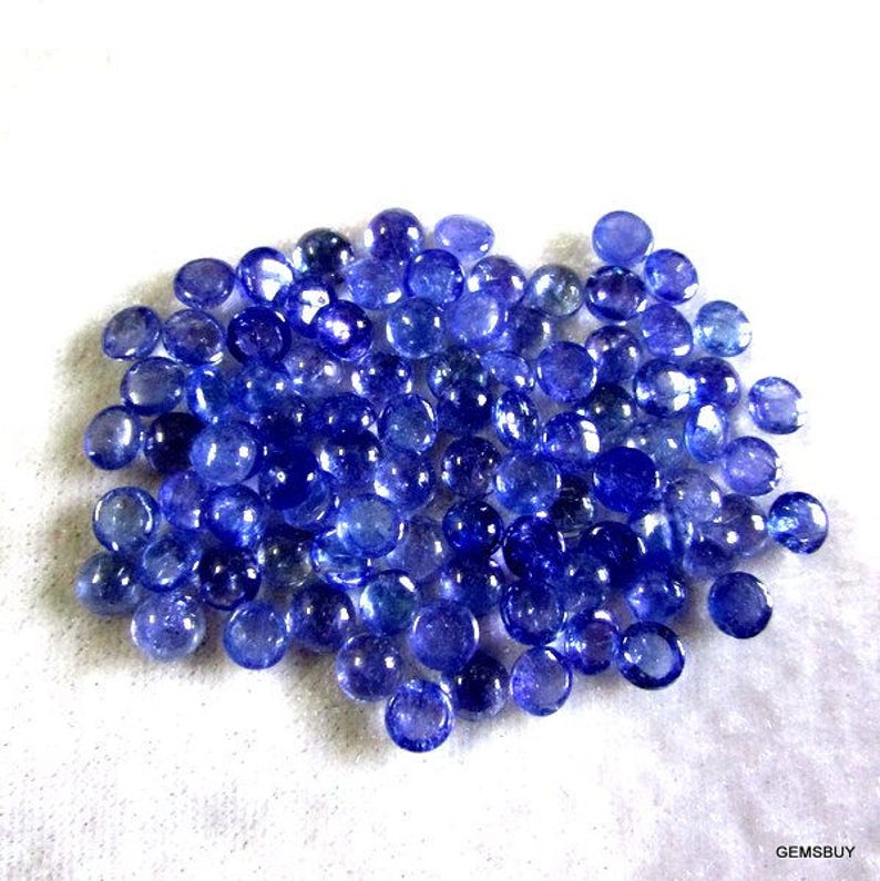 May include: A pile of round, blue gemstones. The gemstones are smooth and have a slight shine. They are all approximately the same size.