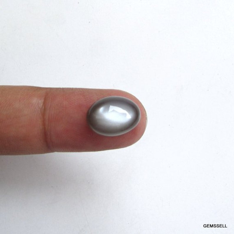 May include: A silver oval cabochon gemstone with a light gray iridescent sheen.