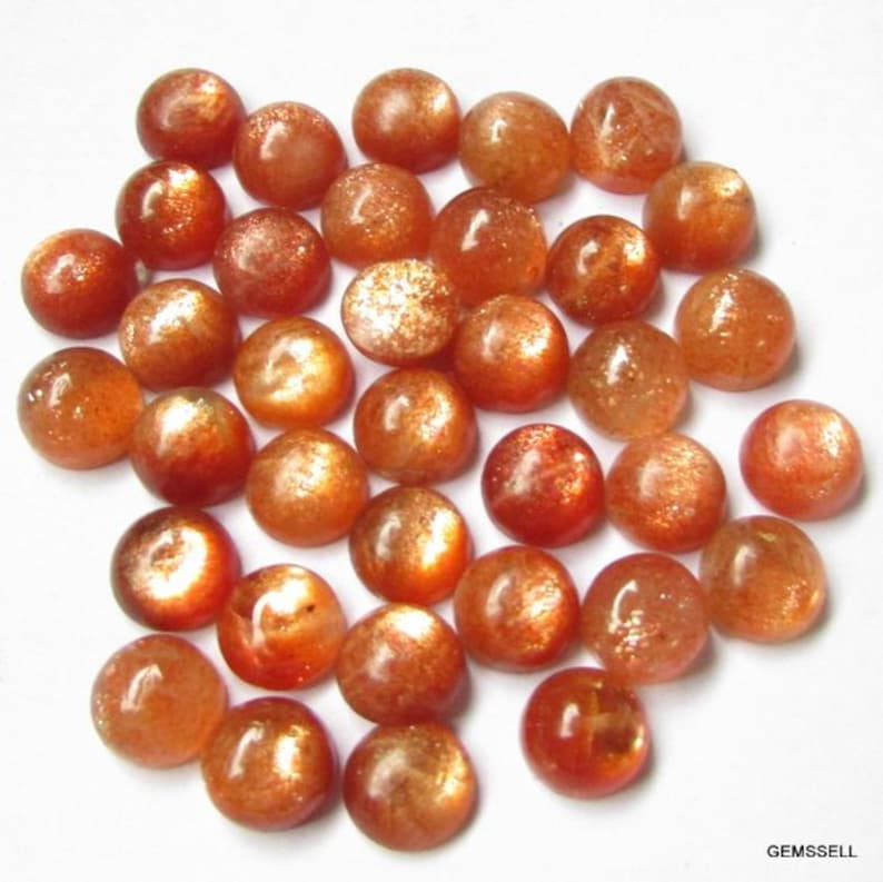 May include: A collection of 30 round, smooth, sunstone cabochons. The stones are a mix of orange, red, and gold colors with a shimmery, iridescent finish.