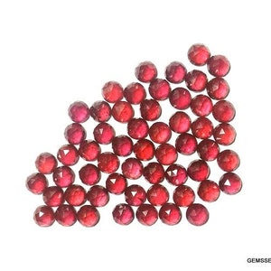 Puede incluir: Una colección de aproximadamente 40 pequeñas piedras preciosas rojas facetadas. Las piedras preciosas están sueltas y dispersas sobre un fondo blanco.