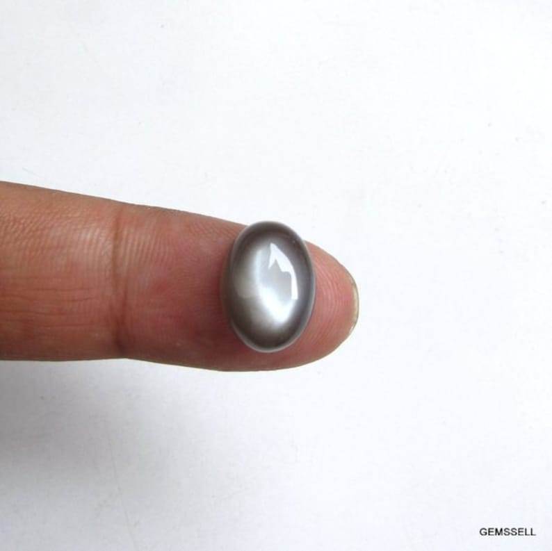 May include: A gray oval cabochon gemstone with a white iridescent sheen.