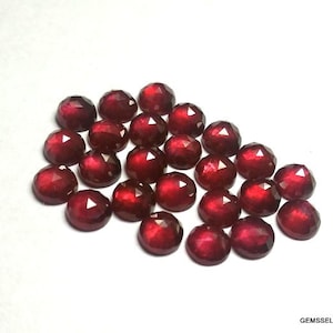May include: A collection of 20 red gemstone cabochons, each with a faceted surface. The stones are arranged in a loose pile on a white background.