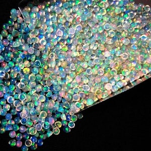Op de afbeelding: Een grote stapel iriserende opaal cabochons in verschillende tinten blauw, groen en roze. De opalen zijn rond en hebben een gladde, gepolijste afwerking.