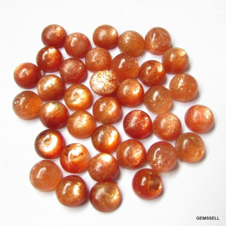 May include: A collection of 30 round, orange-brown sunstone cabochons. The stones are smooth and have a shimmery, iridescent quality.