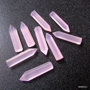 Puede incluir: Diez puntas de cristal rosa, cada una con una punta puntiaguda y una base plana, dispuestas en forma de estrella sobre una superficie negra.