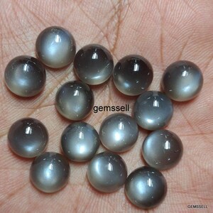 May include: A collection of 14 round, gray moonstone cabochons. The stones have a smooth, polished surface and a subtle shimmer.