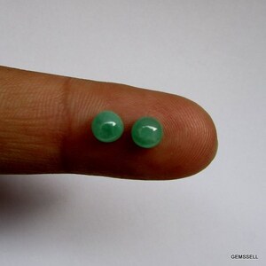 Op de afbeelding: Twee ronde groene edelsteen kralen, ongeveer 5 mm in diameter, worden getoond op een vinger.