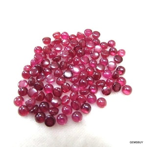 May include: A pile of round, red ruby cabochons. The cabochons are smooth and polished, with a slight sheen.