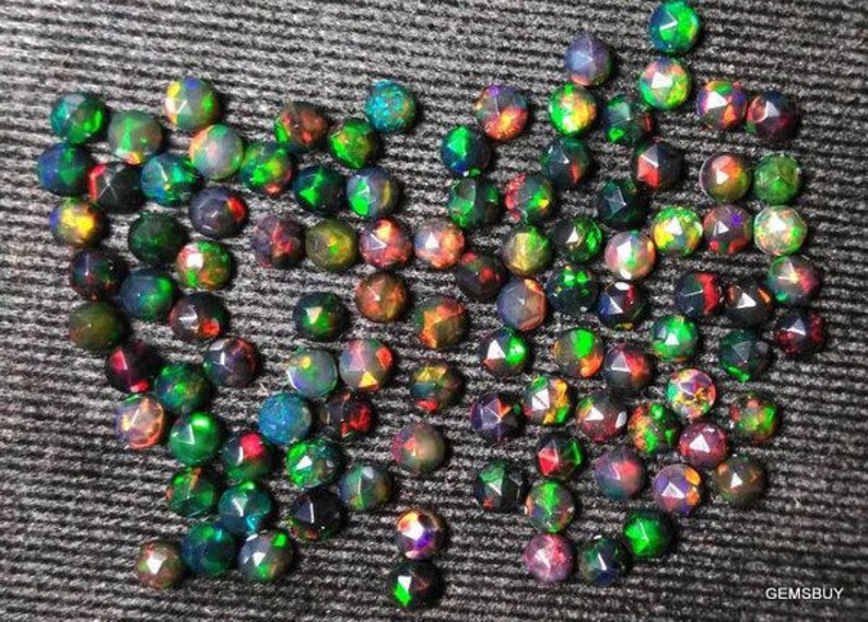 Puede incluir: Una colecci&oacute;n de piedras preciosas de &oacute;palo negro iridiscente, cada una con un patr&oacute;n &uacute;nico de colores verde, rojo y azul. Los &oacute;palos est&aacute;n facetados y tienen una forma puntiaguda.