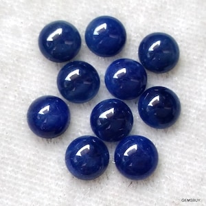 Op de afbeelding: Tien ronde, blauwe saffier cabochons, elk met een glad, gepolijst oppervlak. De cabochons zijn in een losse cluster op een witte achtergrond gerangschikt.