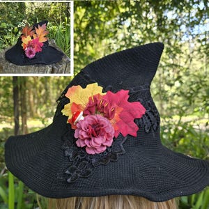 May include: A black witch hat with a wide brim and a pointed crown. The hat is decorated with a large pink flower, fall leaves in shades of red, orange, and yellow, and a small white mushroom.