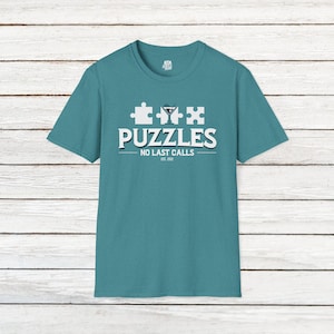 May include: Teal blue t-shirt with a white graphic of puzzle pieces and a martini glass. The text "PUZZLES NO LAST CALLS EST. 2012" is printed below the graphic.