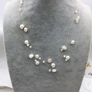 Puede incluir: Un delicado collar de perlas blancas con un diseño de múltiples hilos. Las perlas son de forma y tamaño irregulares, creando un look único y elegante.