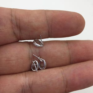 May include: Two silver earring posts with a small oval loop at the top. The posts are designed to hold a charm or pendant.