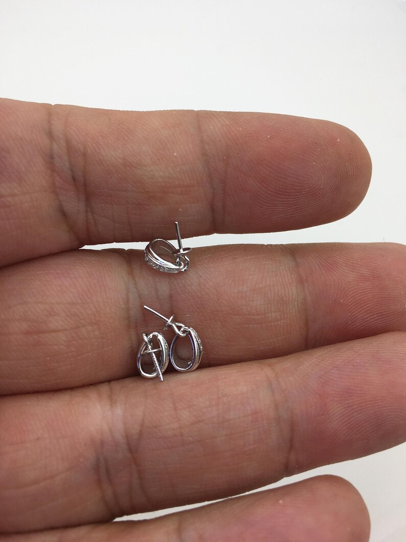 May include: Two silver earring posts with a small oval loop at the top. The posts are designed to hold a charm or pendant.