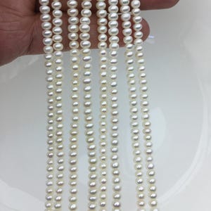 May include: Multiple strands of small, white pearls are shown against a white backdrop. The pearls are round and strung together, likely for necklaces or other jewellery. The pearls have a shiny appearance, reflecting light.
