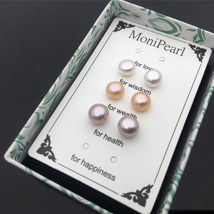 Könnte beinhalten: Eine weiße Schachtel mit grünem Blumendesign enthält eine Karte mit fünf Perlenohrringen. Die Karte trägt den Text "MoniPearl" und listet die Bedeutungen der einzelnen Perlen auf: "für die Liebe", "für Weisheit", "für Reichtum", "für Gesundheit" und "für Glück".
