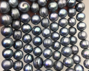Puede incluir: Una colección de perlas redondas de color gris oscuro dispuestas en múltiples hilos verticales. Cada perla presenta una superficie lisa y brillante con sutiles matices iridiscentes y variaciones naturales en la textura, creando un aspecto uniforme.