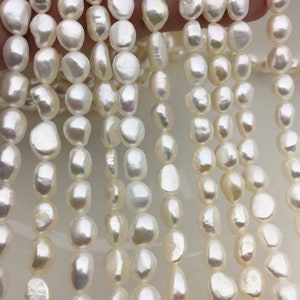 Puede incluir: Una hebra de perlas de agua dulce blancas, cada perla tiene una forma irregular y única. Las perlas están enhebradas en un hilo blanco y están listas para ser utilizadas en la elaboración de joyas.
