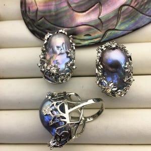 May include: Three silver rings with a baroque pearl set in each. The pearls are a dark iridescent blue-grey color. The rings are set with small white stones.