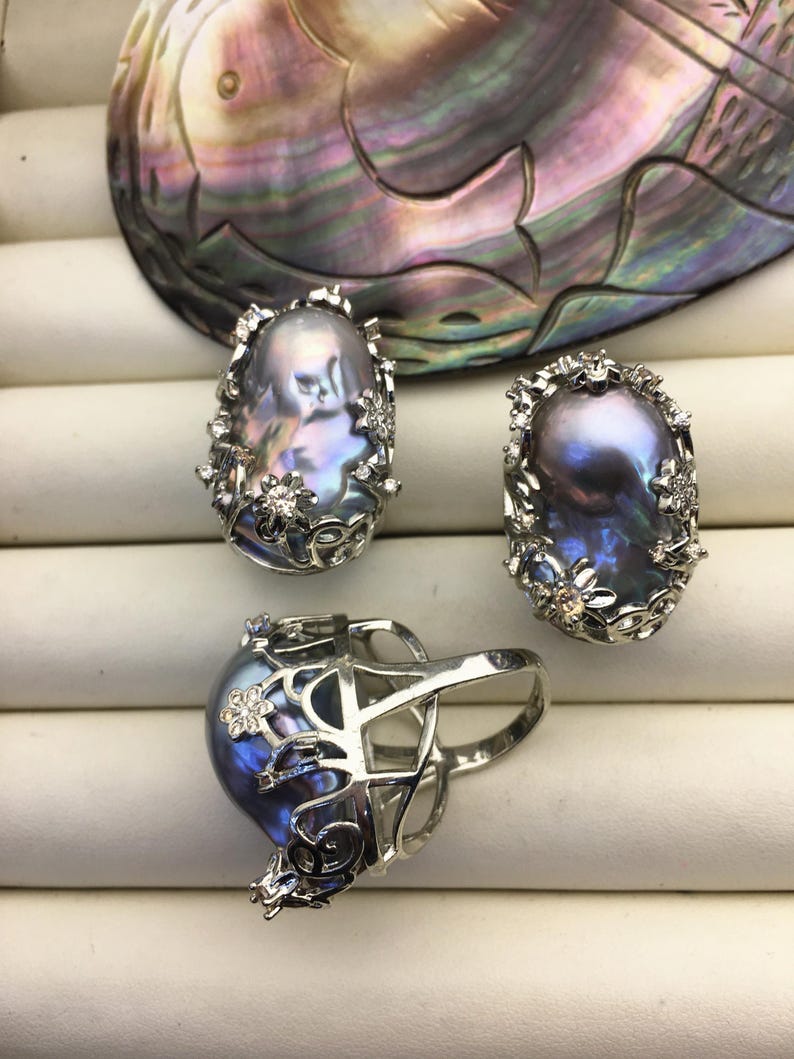May include: Three silver rings with a baroque pearl set in each. The pearls are a dark iridescent blue-grey color. The rings are set with small white stones.