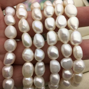 May include: A strand of white freshwater pearls, with a smooth, slightly irregular shape. The pearls are strung on a clear thread and are arranged in a loose, flowing pattern.